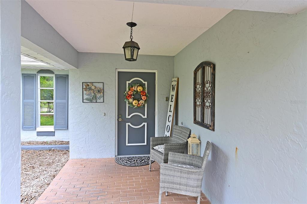 A covered front porch features a gray door, two wicker chairs, and brick flooring — 811 ALDERWOOD WAY, SARASOTA, FL