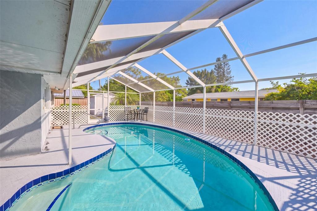 A swimming pool enclosed by a white screen cage sits on a concrete patio — 811 ALDERWOOD WAY, SARASOTA, FL