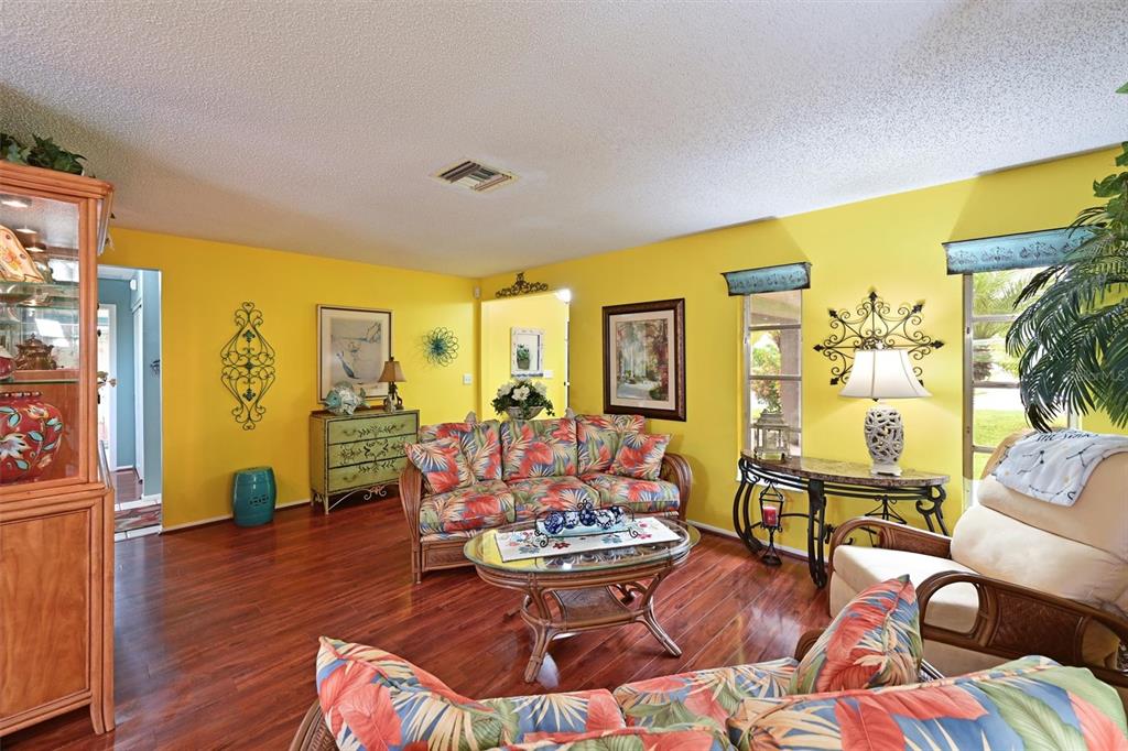 A living room with yellow walls, hardwood floors, and tropical-patterned furniture — 811 ALDERWOOD WAY, SARASOTA, FL