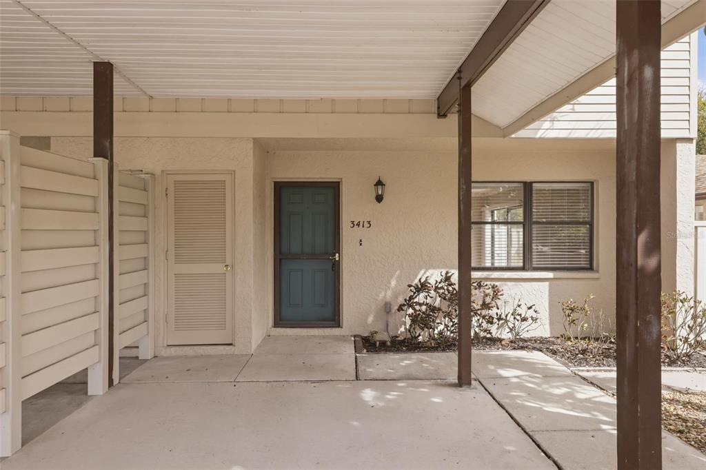 A covered concrete entryway features a blue front door, a louvered utility door, and posts — 3413 51ST AVENUE CIRCLE W UNIT 205, BRADENTON, FL
