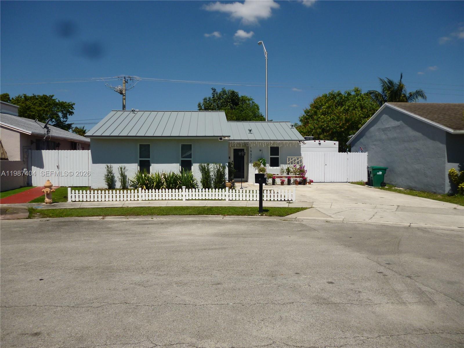 A single-story house with a metal roof and a white picket fence in front — 19372 SW 119th Ct, Miami FL 33177, MIAMI, FL