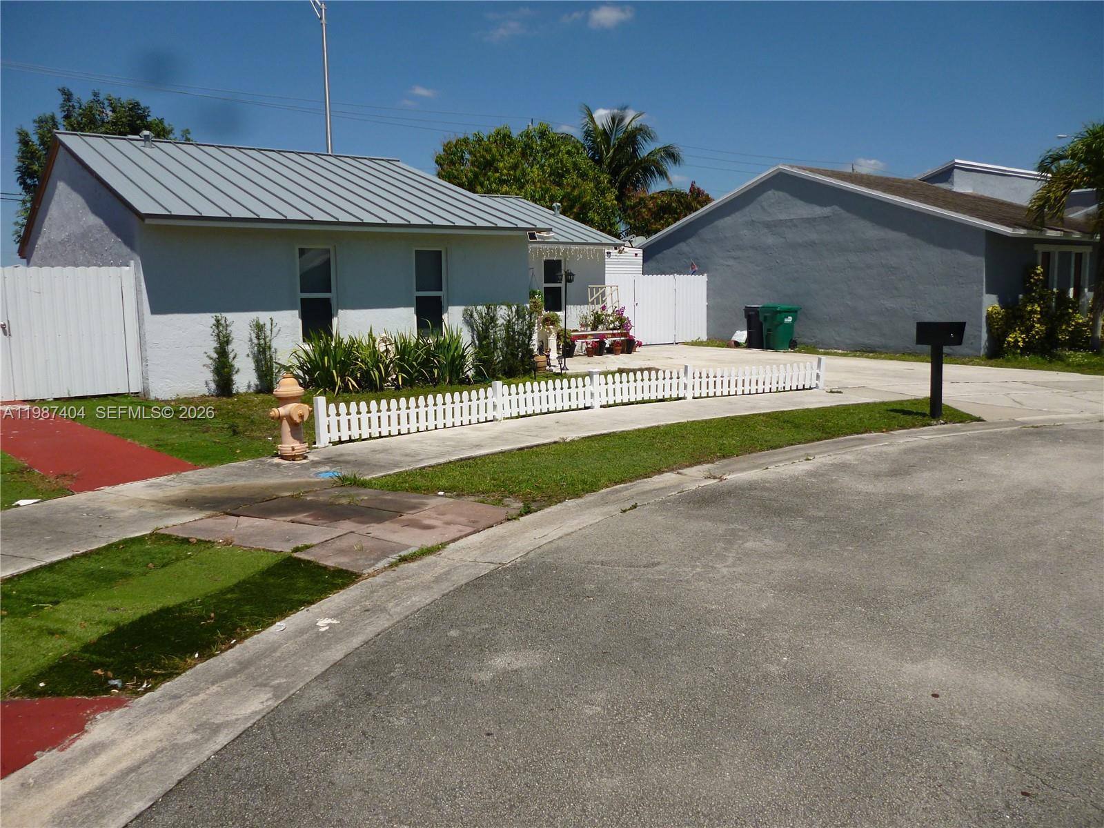 A single-story house with a metal roof and a white picket fence in front — 19372 SW 119th Ct, Miami FL 33177, MIAMI, FL