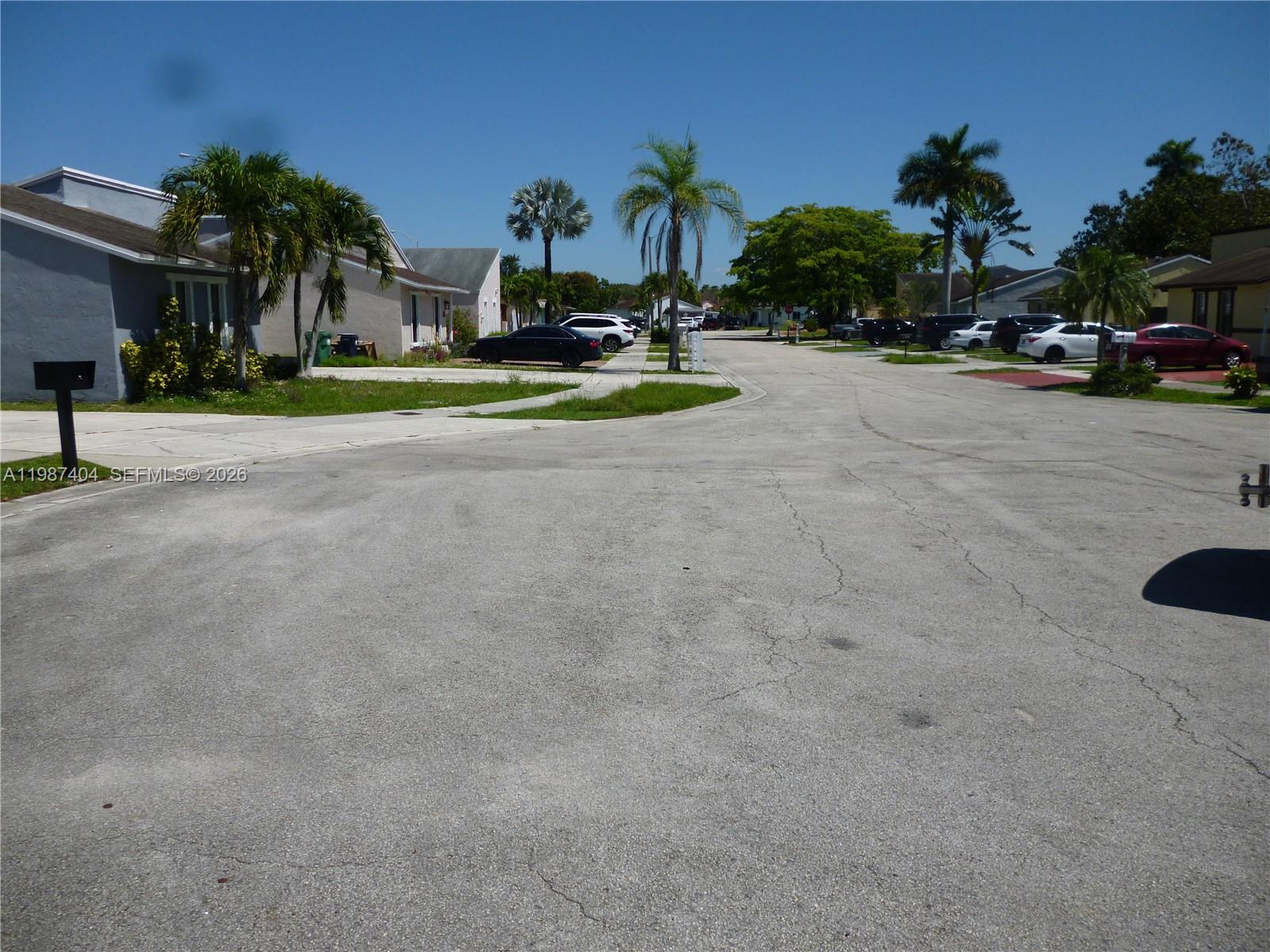 A residential street scene features houses, palm trees, and parked cars under a clear sky — 19372 SW 119th Ct, Miami FL 33177, MIAMI, FL
