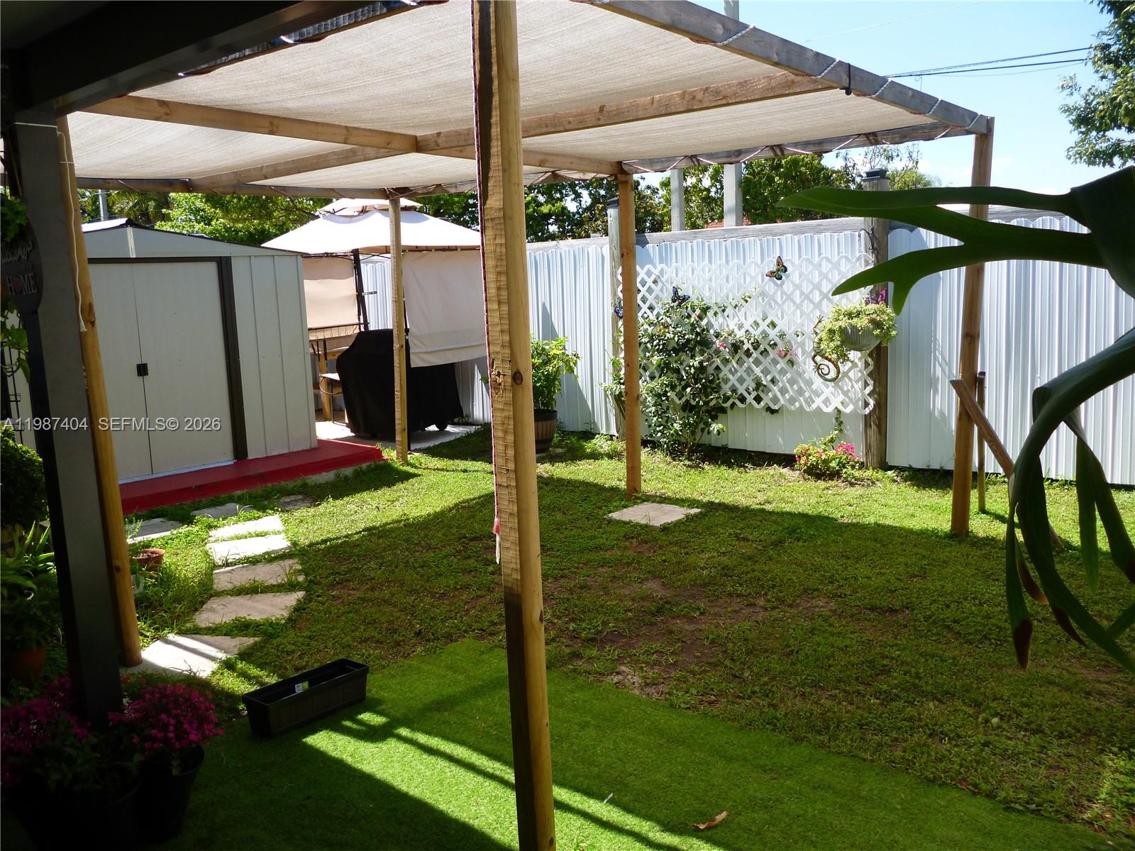 A backyard features a wooden pergola with a shade cloth, a storage shed, and landscaping — 19372 SW 119th Ct, Miami FL 33177, MIAMI, FL