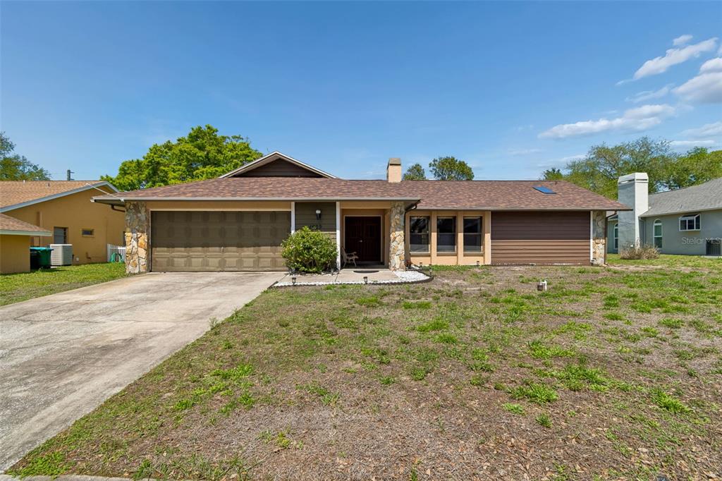 A single-story house with a brown roof, stone accents, and a large front yard — 1039 NORTHRIDGE DRIVE, PALM HARBOR, FL