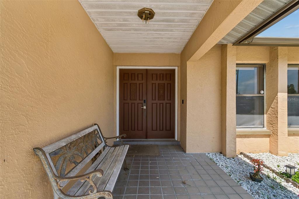 A covered entryway features a tiled porch, a wooden bench, and double front doors — 1039 NORTHRIDGE DRIVE, PALM HARBOR, FL