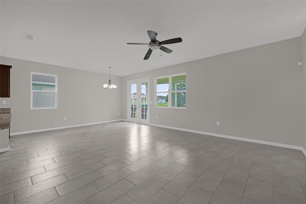 A spacious, empty room features gray tile flooring, light gray walls, a ceiling fan, and French doors — 12112 CARSON DRIVE, ORLANDO, FL