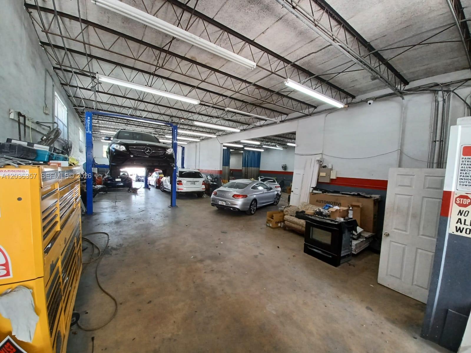 An automotive repair shop features a car lift, multiple vehicles, and concrete flooring — 707 N Dixie Hwy, Hallandale Beach FL 33009, HALLANDALE BEACH, FL