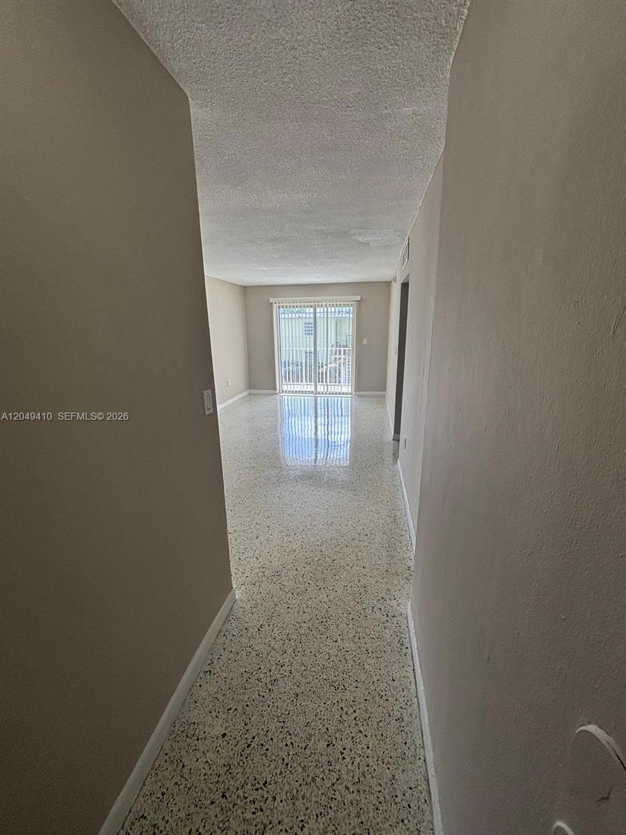 A hallway with terrazzo flooring leads to a living area with sliding glass doors — 1047 SW 7th St # 12, Miami FL 33130, MIAMI, FL