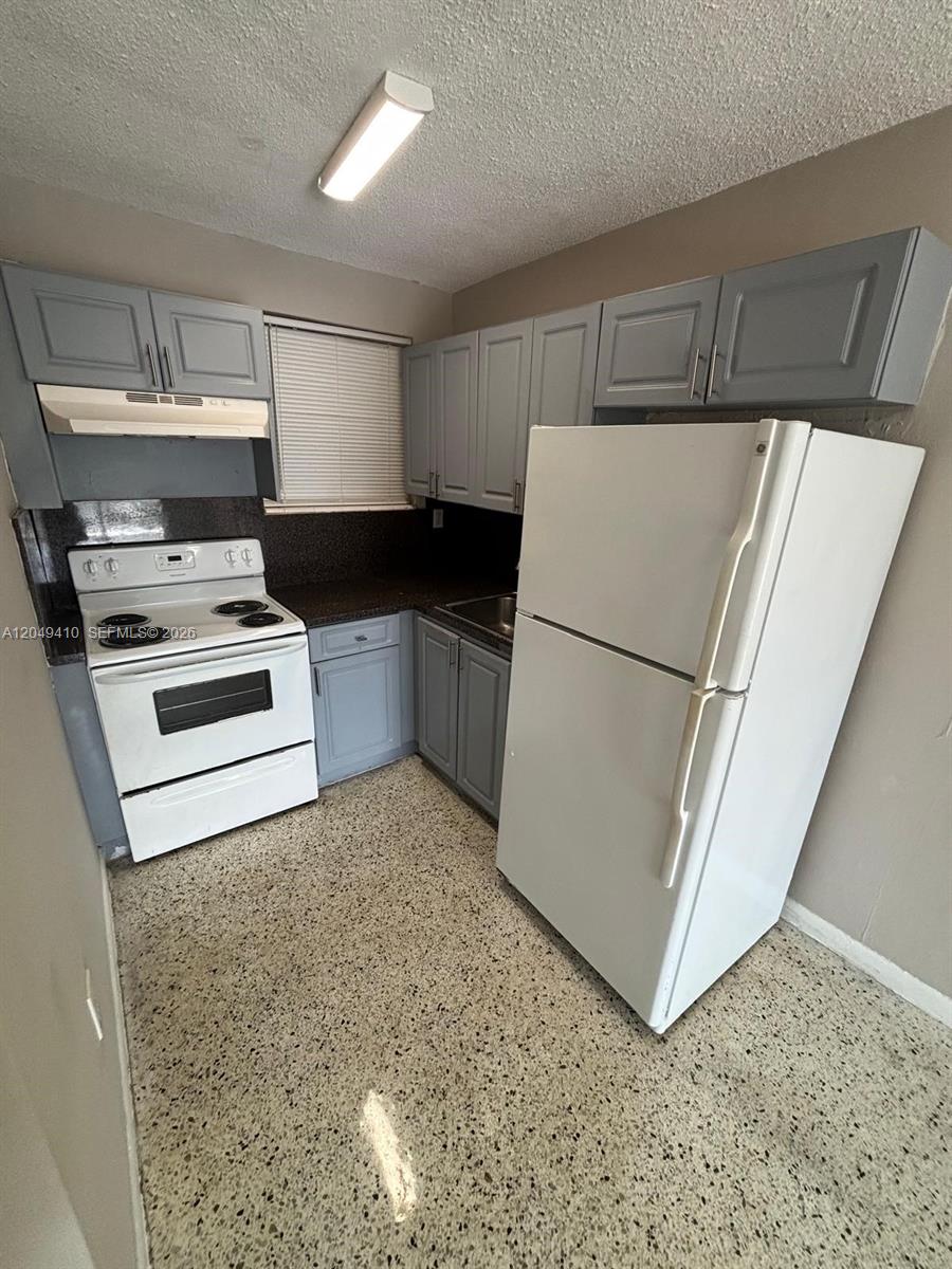 A small kitchen features gray cabinets, a white stove, a white refrigerator, and speckled flooring — 1047 SW 7th St # 12, Miami FL 33130, MIAMI, FL
