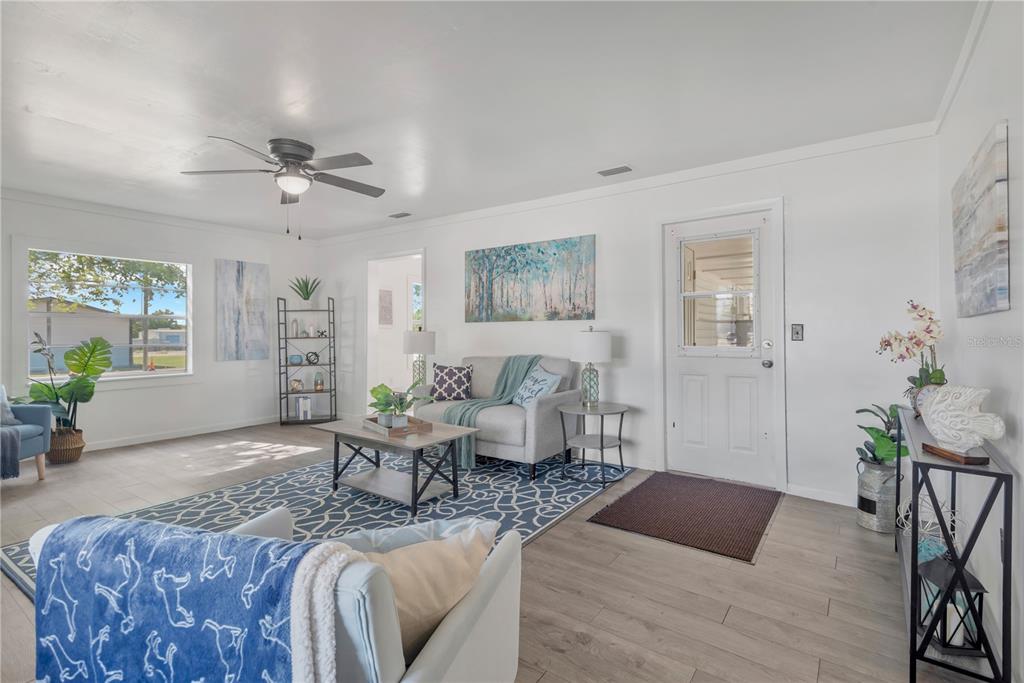 A bright living room features light wood-look flooring, a ceiling fan, and a blue area rug — 216 LANGFORD STREET NW, FORT MEADE, FL