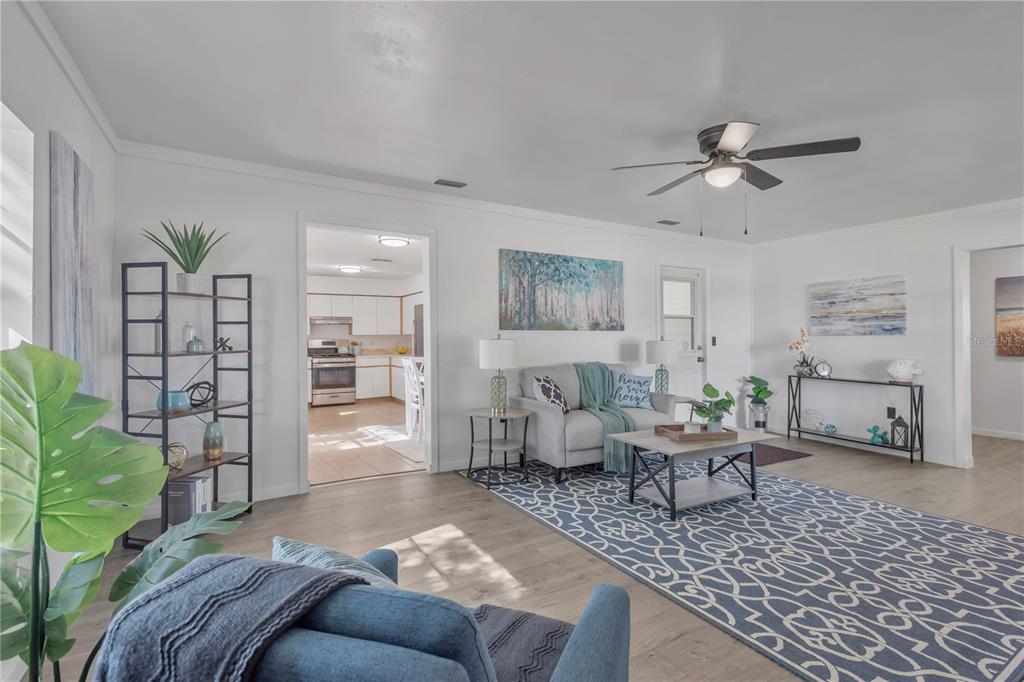 A living room with light wood floors, a blue patterned rug, and an adjacent kitchen — 216 LANGFORD STREET NW, FORT MEADE, FL
