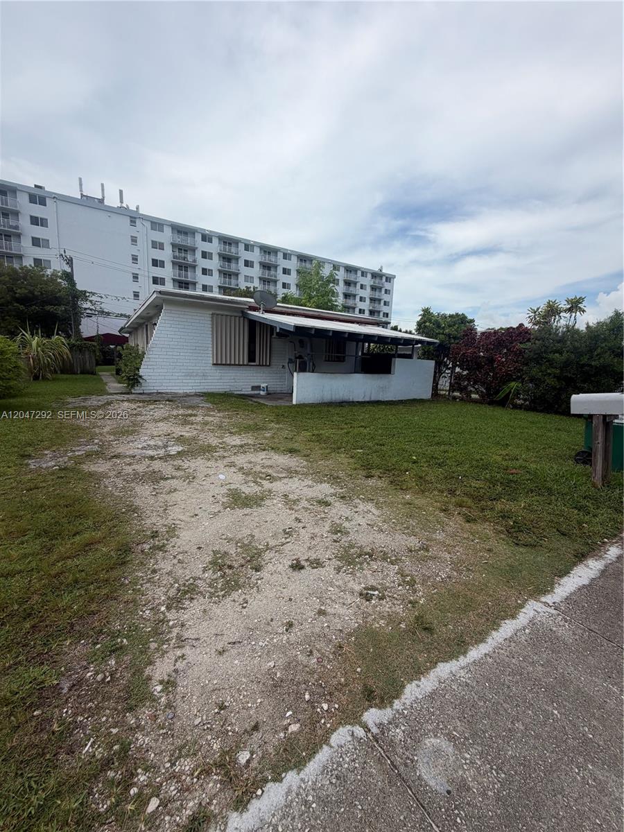A white, single-story house with a gravel driveway sits in front of a large apartment building — 1258 NE 109th St, Miami FL 33161, MIAMI, FL