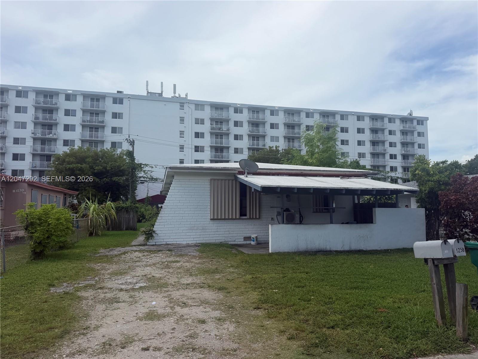A white single-story house with a flat roof stands in front of a large apartment building — 1258 NE 109th St, Miami FL 33161, MIAMI, FL