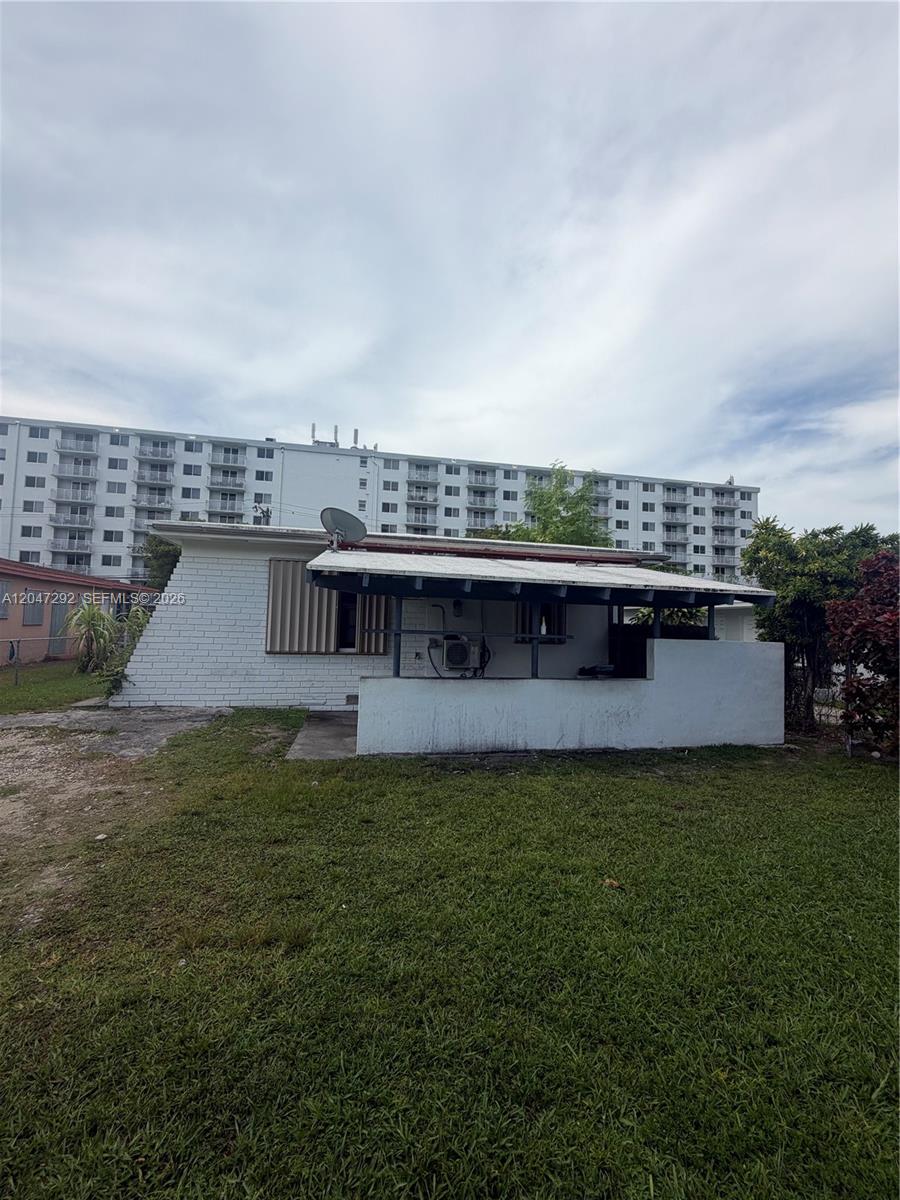 A single-story white brick house features a covered patio and a large apartment building behind — 1258 NE 109th St, Miami FL 33161, MIAMI, FL