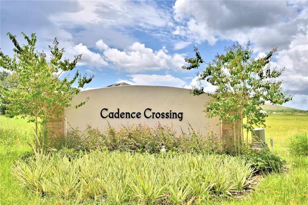 A beige neighborhood entrance sign reading Cadence Crossing sits surrounded by grass and trees — 4430 JUNEBERRY DRIVE, AUBURNDALE, FL