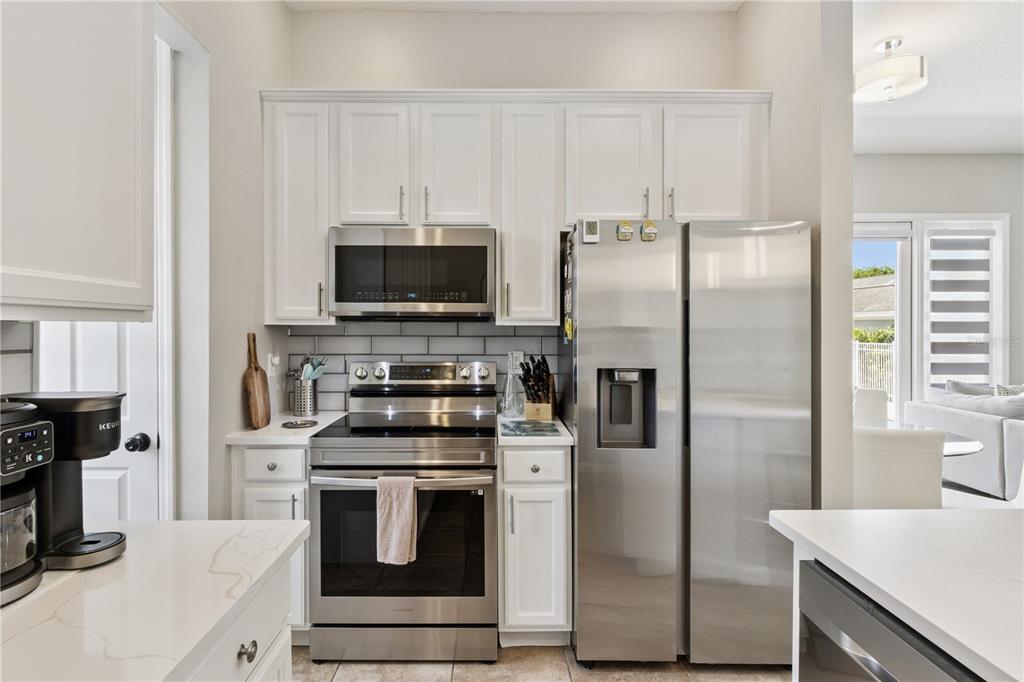 A kitchen features white cabinets, stainless steel appliances, and a gray subway tile backsplash — 7407 OCONEE ST, REUNION, FL
