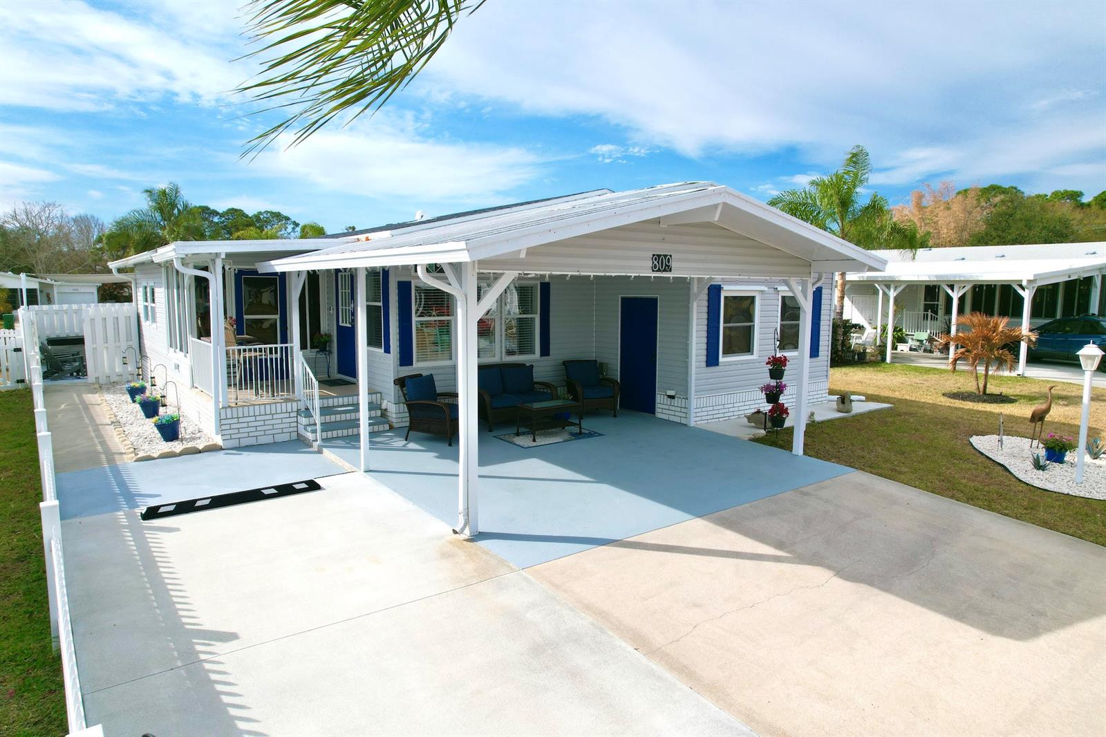 A light-colored mobile home features a covered carport, a front porch, and blue shutters — 809 Lychee Drive, Barefoot Bay FL 32976, BAREFOOT BAY, FL