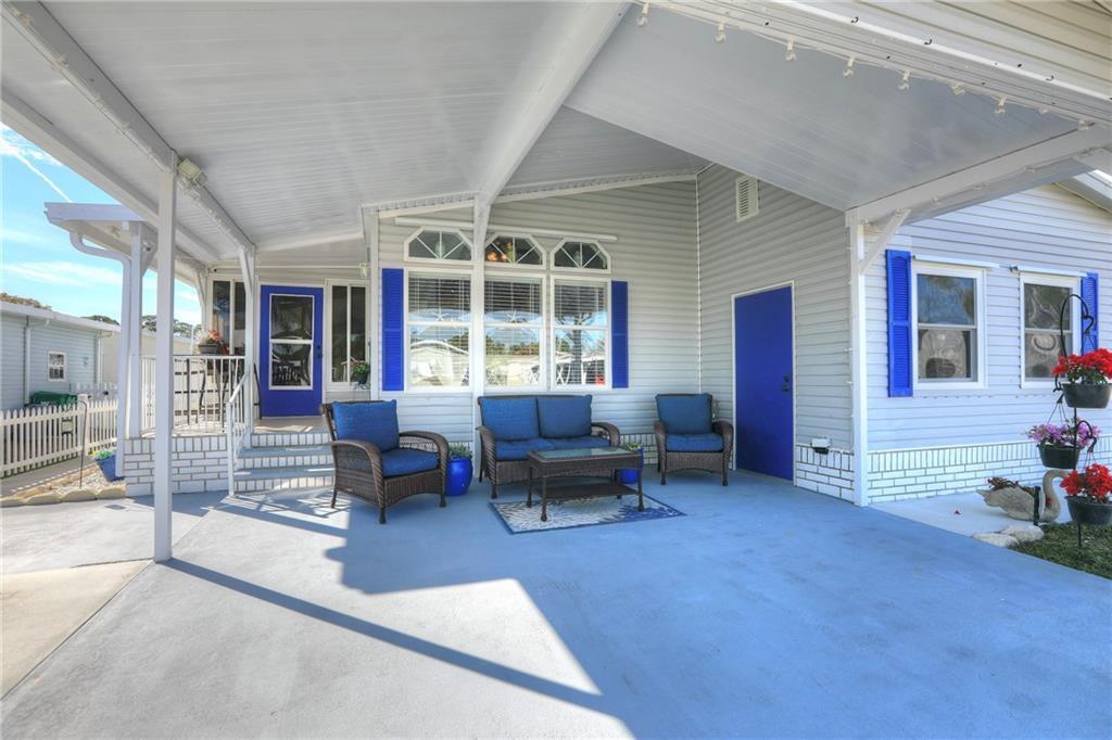 A covered patio features light gray siding, blue shutters, a blue door, and outdoor furniture — 809 Lychee Drive, Barefoot Bay FL 32976, BAREFOOT BAY, FL