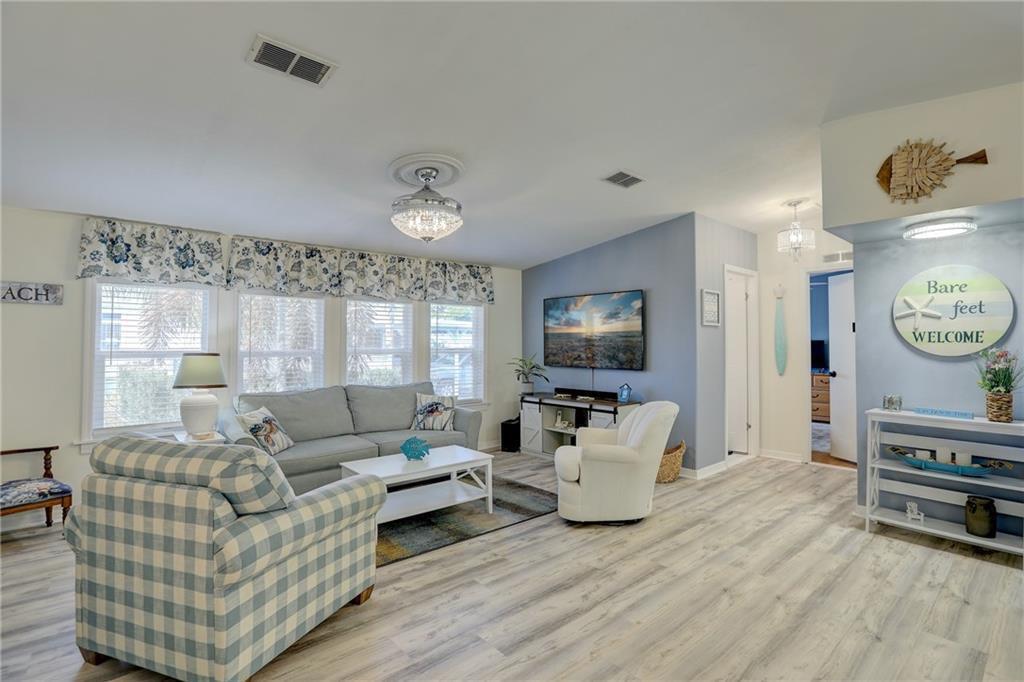 A living room features light wood-look flooring, a blue accent wall, and coastal decor — 809 Lychee Drive, Barefoot Bay FL 32976, BAREFOOT BAY, FL