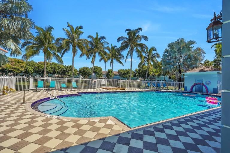 A swimming pool with a checkered deck is surrounded by palm trees and a fence — 1942 Alamanda Way, Riviera Beach FL 33404, RIVIERA BEACH, FL