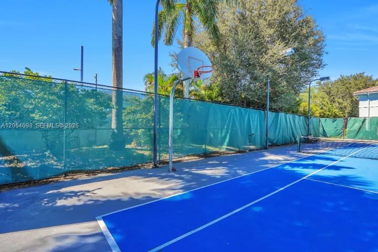 A basketball hoop stands on a blue outdoor court enclosed by a green privacy fence — 1942 Alamanda Way, Riviera Beach FL 33404, RIVIERA BEACH, FL