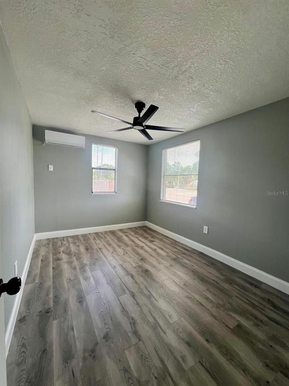 An empty bedroom features gray walls, wood-look flooring, a ceiling fan, and a wall-mounted AC unit — 708 MARTIN L KING JR AVENUE, LAKELAND, FL