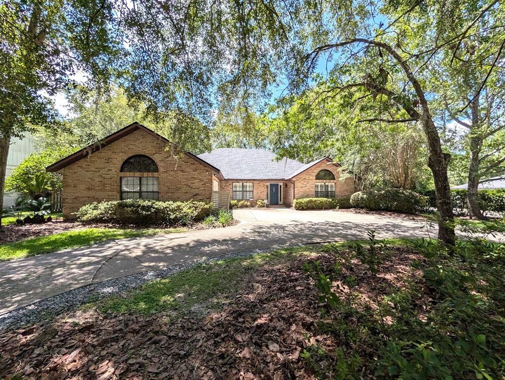 A single-story brick house with a large driveway sits behind trees on a sunny day — 6124 SW 35TH WAY, GAINESVILLE, FL