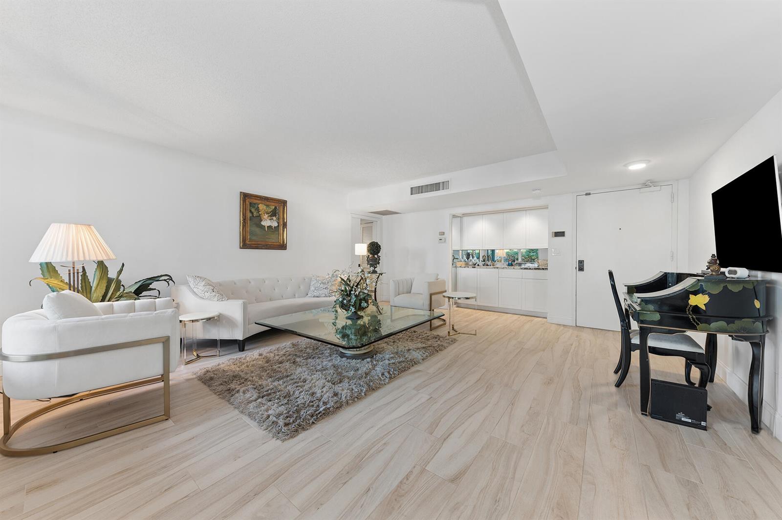 A modern living room features a white sofa, glass coffee table, and light wood flooring — 100 SE 5th Avenue # 102, Boca Raton FL 33432, BOCA RATON, FL
