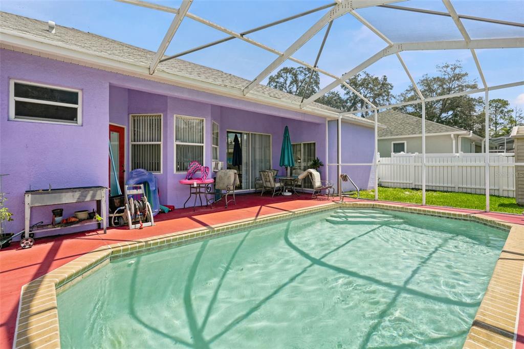 A swimming pool with a screened-in enclosure sits on a red patio beside a purple house — 15486 SARATOGA DRIVE, BROOKSVILLE, FL