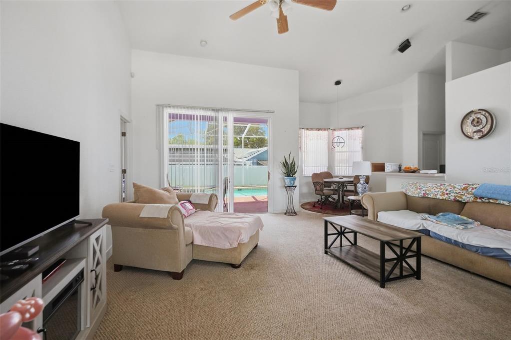 A living room with carpeted floors, a television, a sofa, and a sliding glass door — 15486 SARATOGA DRIVE, BROOKSVILLE, FL
