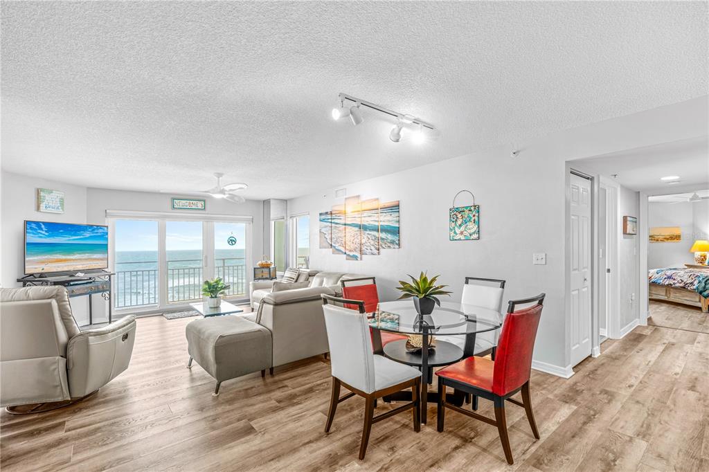 A bright living and dining area features wood-look flooring, a glass-top table, and ocean views — 2967 S ATLANTIC AVENUE UNIT 903, DAYTONA BEACH SHORES, FL