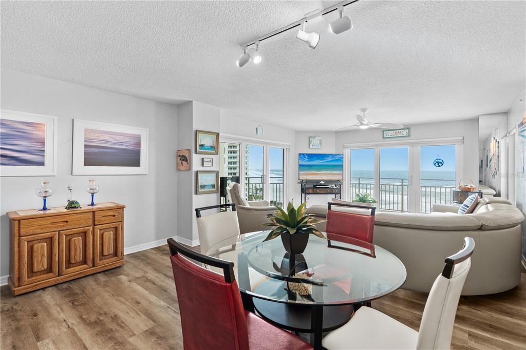 A dining area with a glass table and red chairs opens to a living room — 2967 S ATLANTIC AVENUE UNIT 903, DAYTONA BEACH SHORES, FL