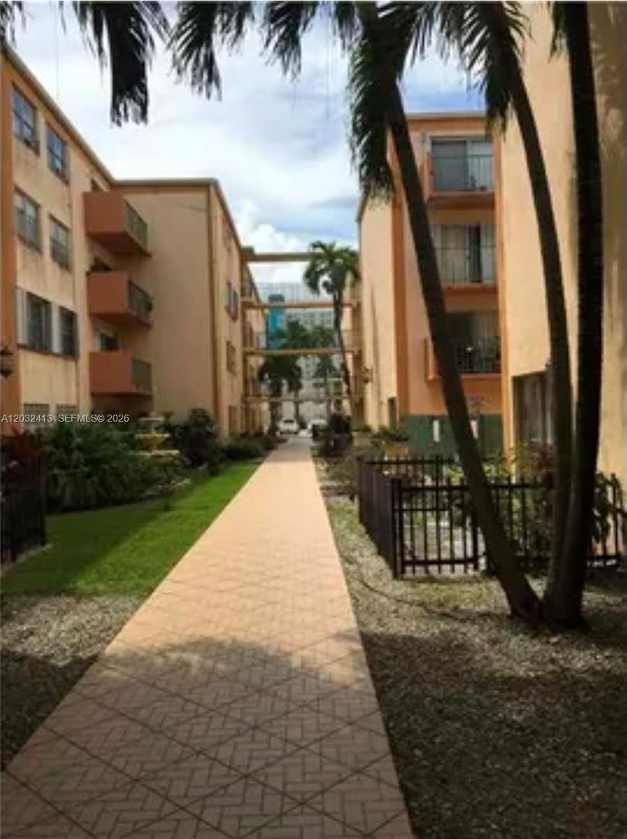 A paved walkway leads between two multi-story apartment buildings with palm trees and landscaping — 5501 NW 7th St # E408, Miami FL 33126, MIAMI, FL