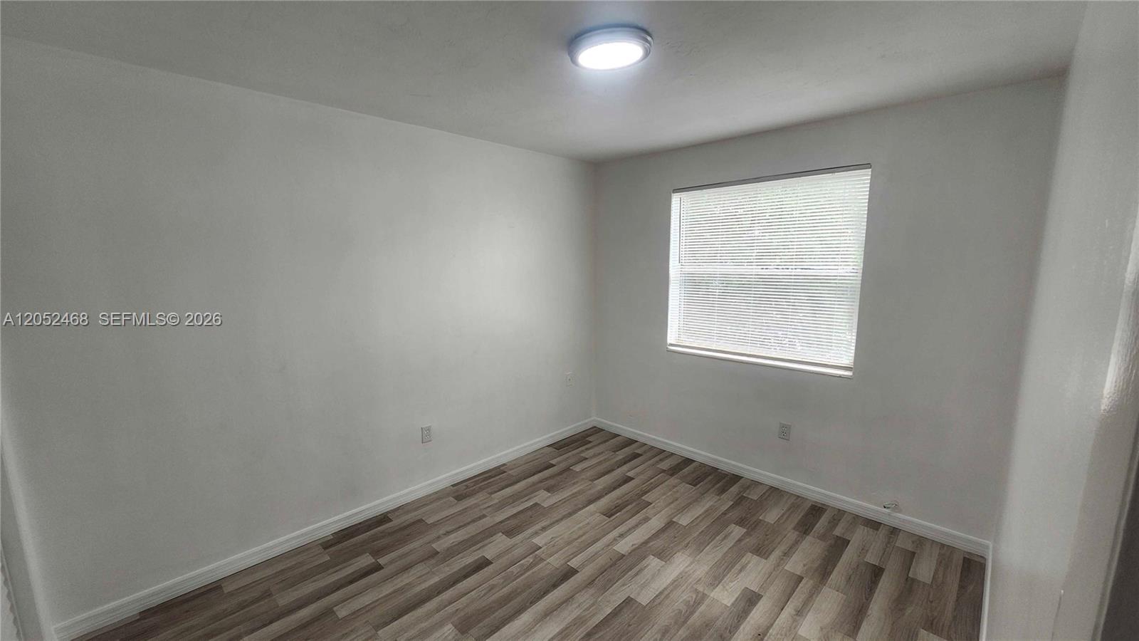 An empty bedroom features white walls, a single window with blinds, and wood-look flooring — 111 NW 152nd St # 16, Miami FL 33169, MIAMI, FL