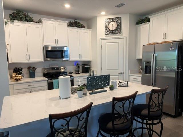A kitchen features white cabinets, a quartz island with seating, and stainless steel appliances — 9760 MINNOW RAY DRIVE, LAND O LAKES, FL