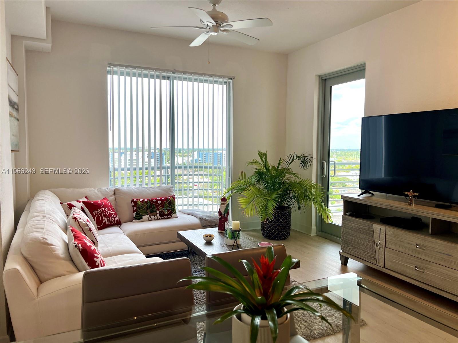 A living room features a white sectional sofa, a television console, and a balcony door — 1830 Radius Dr # 1203, Hollywood FL 33020, HOLLYWOOD, FL