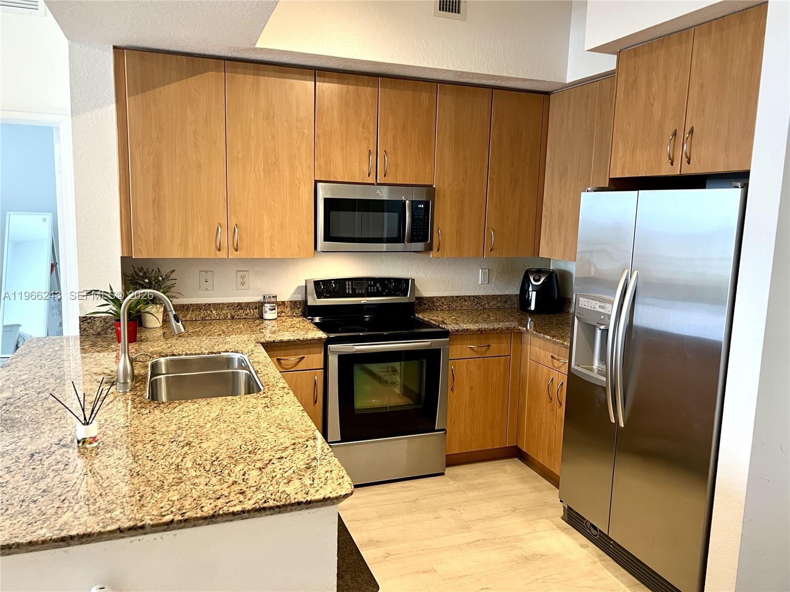 A kitchen features light wood cabinets, granite countertops, and stainless steel appliances — 1830 Radius Dr # 1203, Hollywood FL 33020, HOLLYWOOD, FL