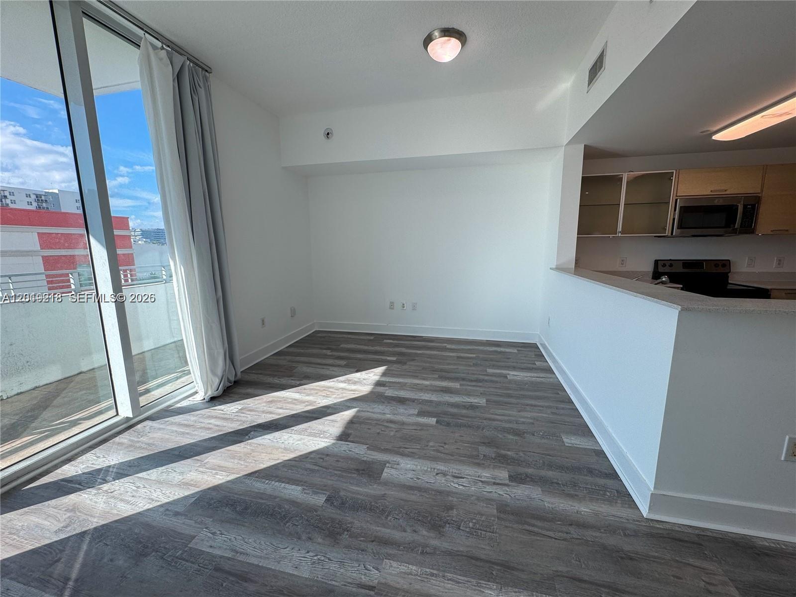 An empty living area features wood-look flooring, white walls, and a sliding glass balcony door — 350 NE 24th St # 514, Miami FL 33137, MIAMI, FL