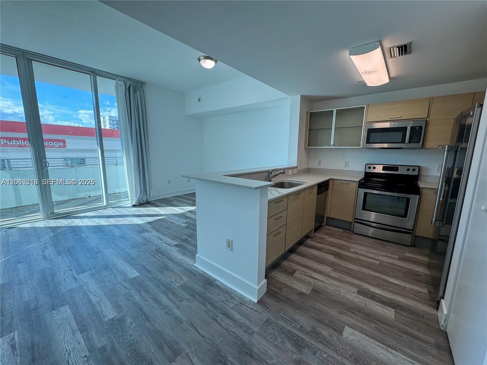 A kitchen with stainless steel appliances and light wood cabinets opens to a living area — 350 NE 24th St # 514, Miami FL 33137, MIAMI, FL