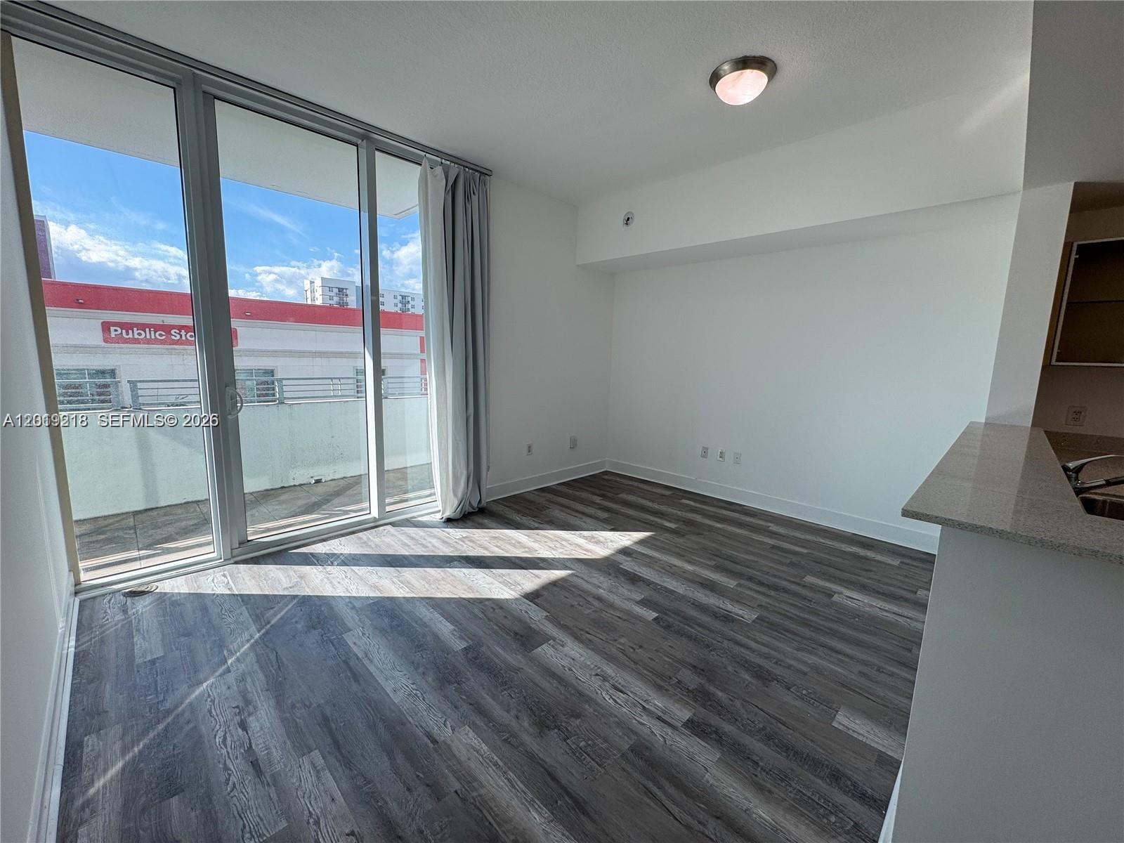 A bright room features wood-look flooring, a sliding glass door, and a view of a building — 350 NE 24th St # 514, Miami FL 33137, MIAMI, FL