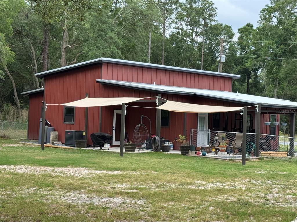 A red metal-sided building features a covered patio with shade sails and a grassy yard — 8031 NW 172ND LANE, FANNING SPRINGS, FL