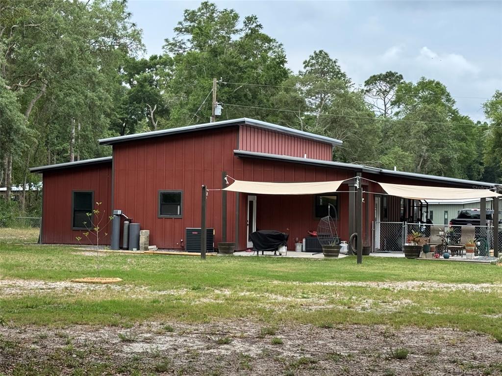 A red metal-sided house with a flat roof and a patio covered by shade sails — 8031 NW 172ND LANE, FANNING SPRINGS, FL