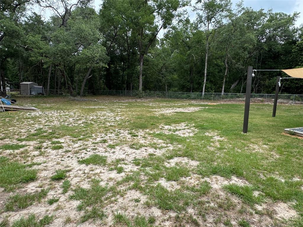A large, grassy backyard features patches of sand and is enclosed by a chain-link fence — 8031 NW 172ND LANE, FANNING SPRINGS, FL