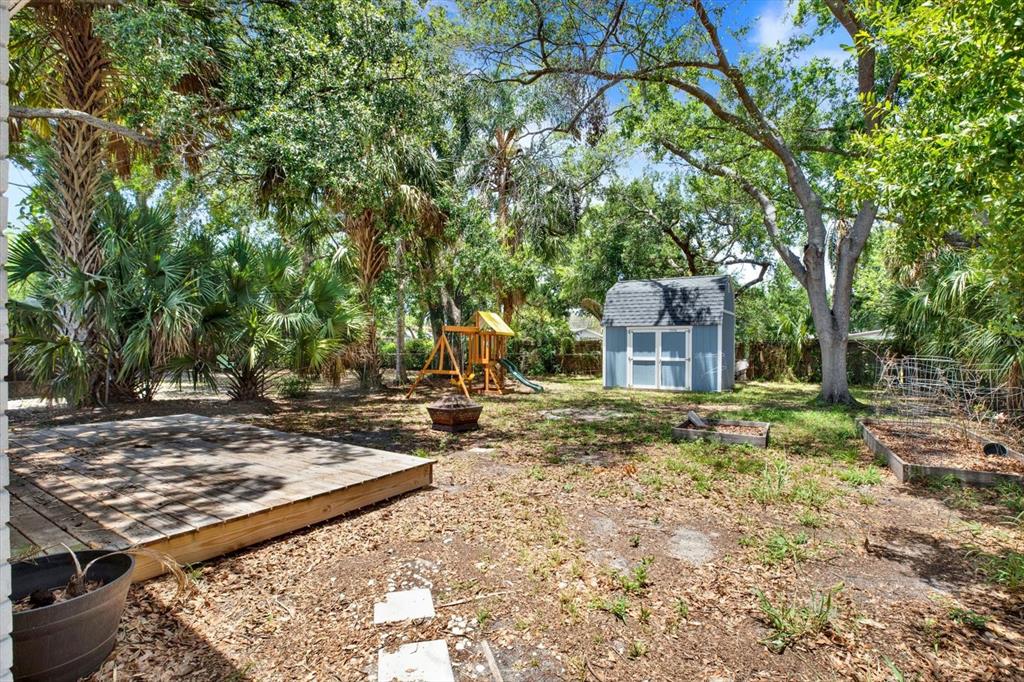 A backyard features a wooden deck, a shed, a playground set, and mature trees — 3813 W WISCONSIN AVENUE, TAMPA, FL
