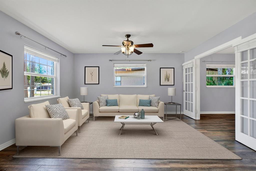 A living room with light gray walls, white furniture, a ceiling fan, and wood flooring — 3813 W WISCONSIN AVENUE, TAMPA, FL