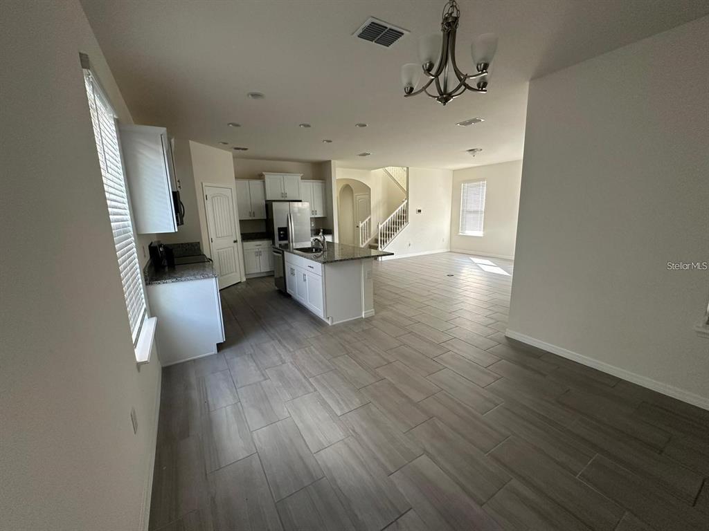An open-concept kitchen with white cabinets, granite countertops, and tile flooring leads to stairs — 17865 ADRIFT ROAD, WINTER GARDEN, FL
