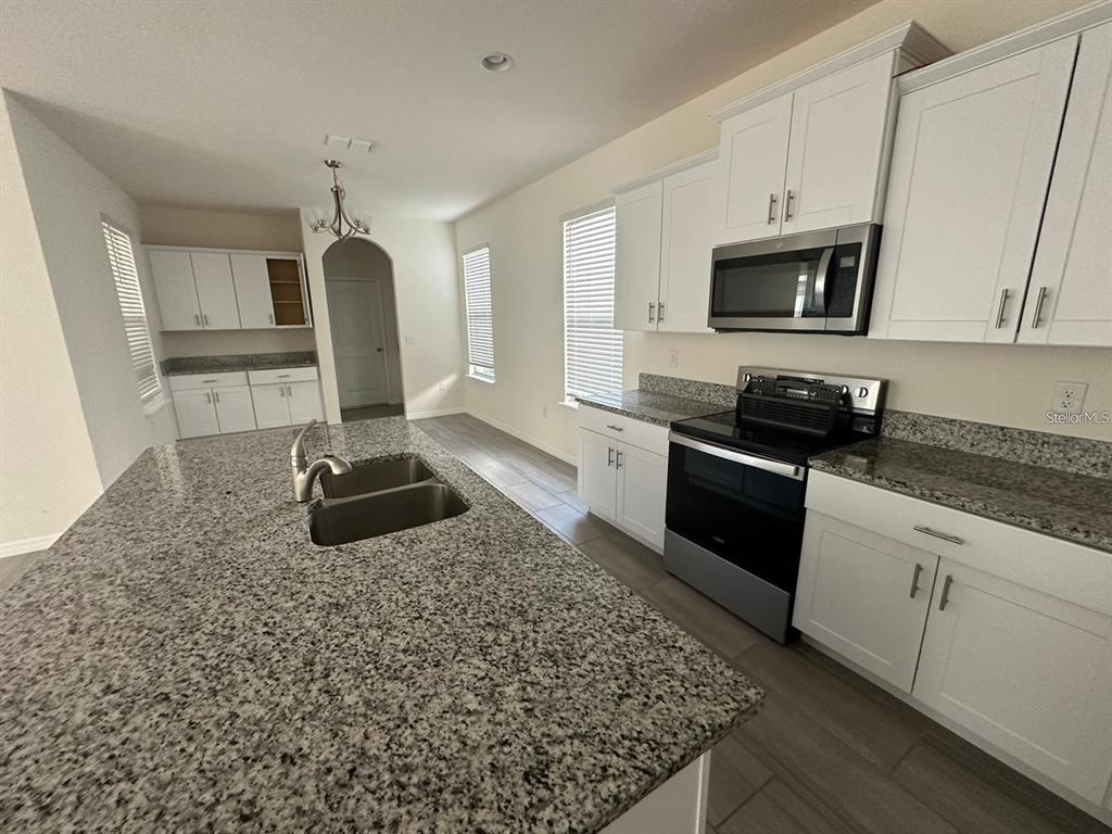 A kitchen features white cabinets, granite countertops, a large island with a sink, and appliances — 17865 ADRIFT ROAD, WINTER GARDEN, FL