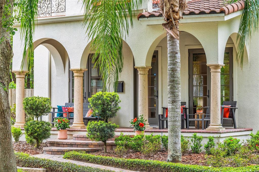 A Mediterranean-style home features a covered porch with arched openings, stone columns, and patio furniture — 18 CELIA LANE, ORLANDO, FL