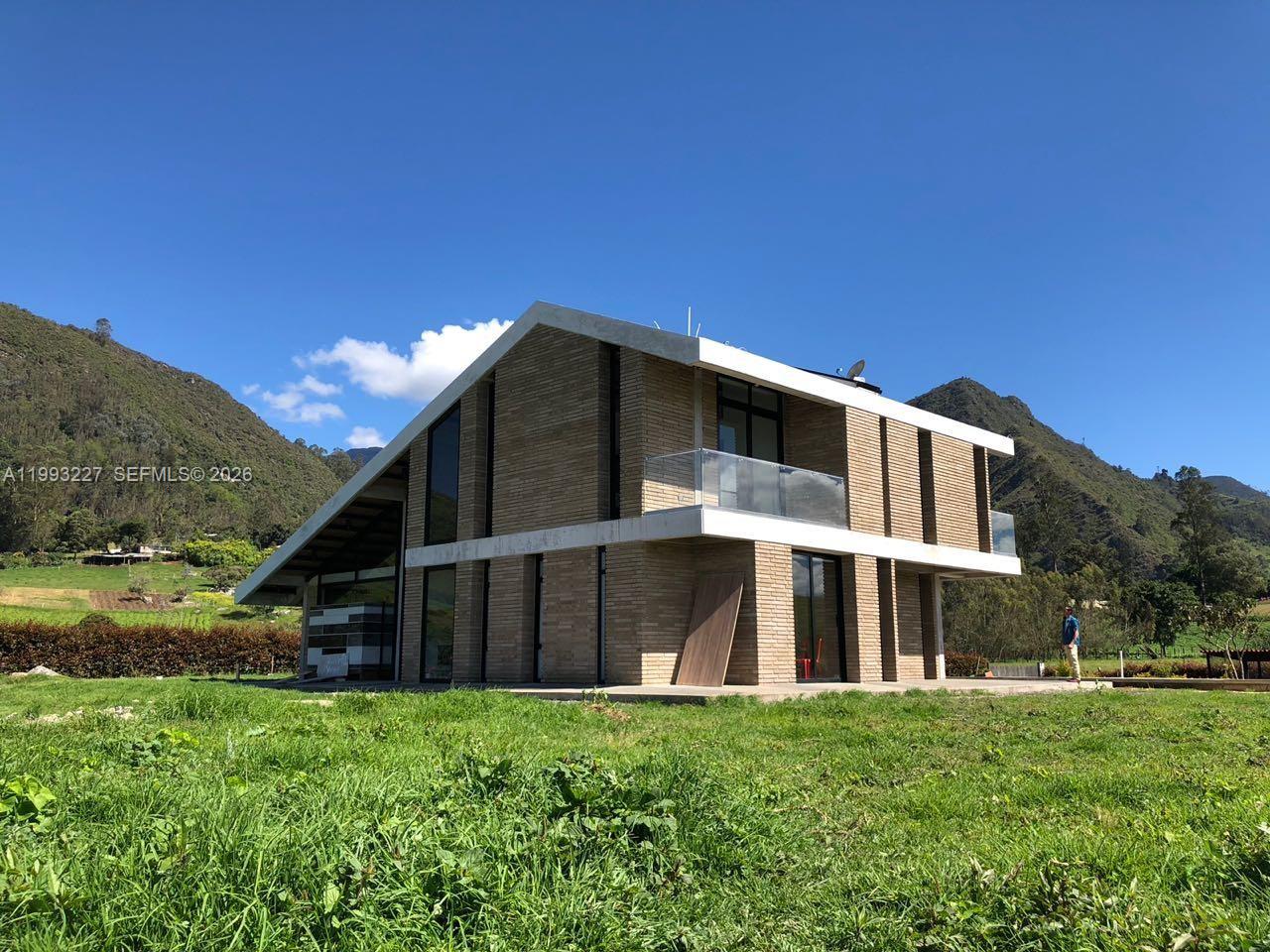 A modern two-story brick house with a sloped roof sits in a grassy field — 4.2 KILOMETRO NW VEREDA BOBADILLAS, Bg, Bg